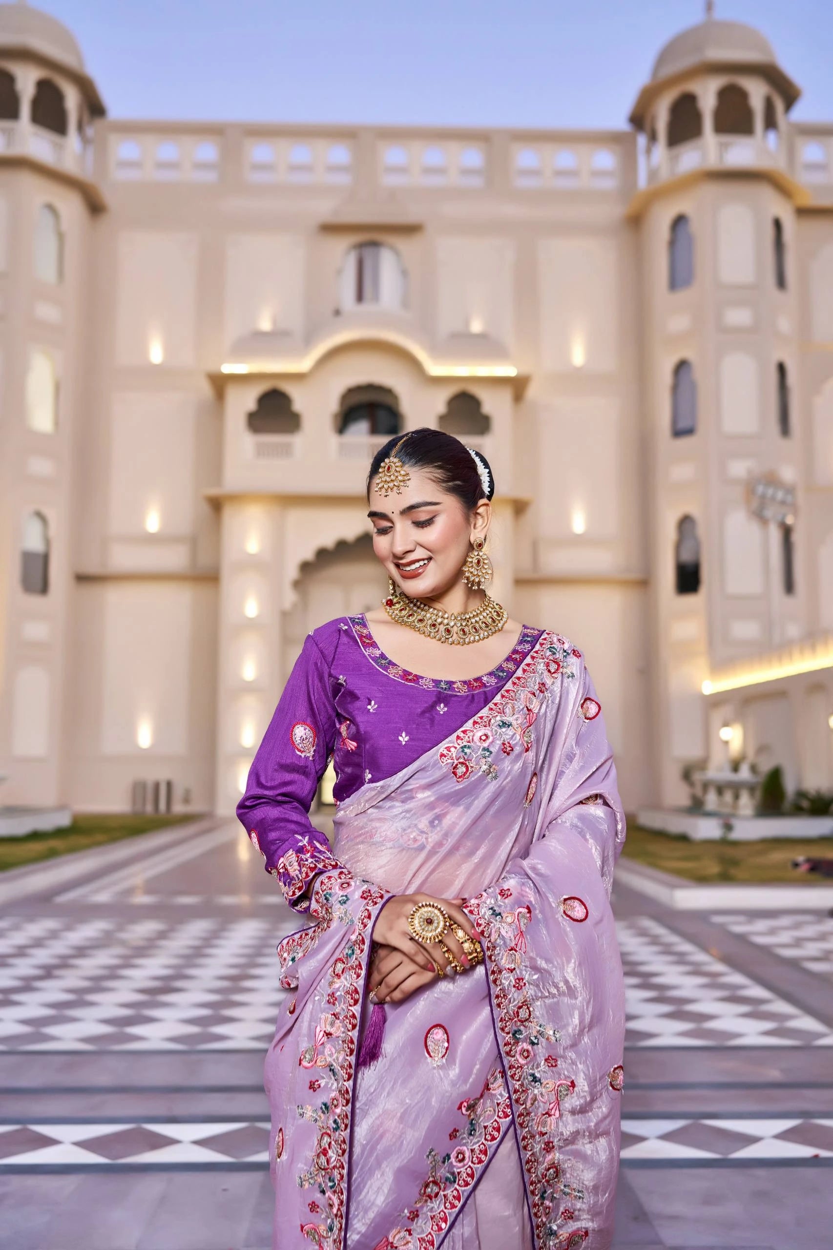 Woman in a purple saree standing in front of an architectural building.